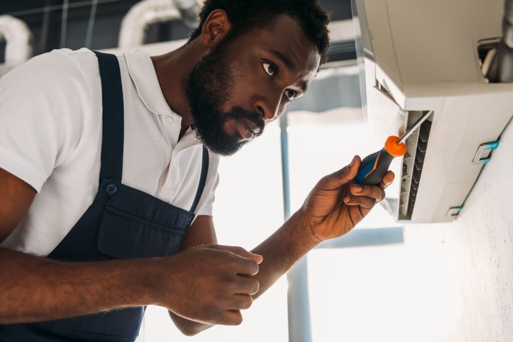 African american repairman fixing air conditioner with screwdriver