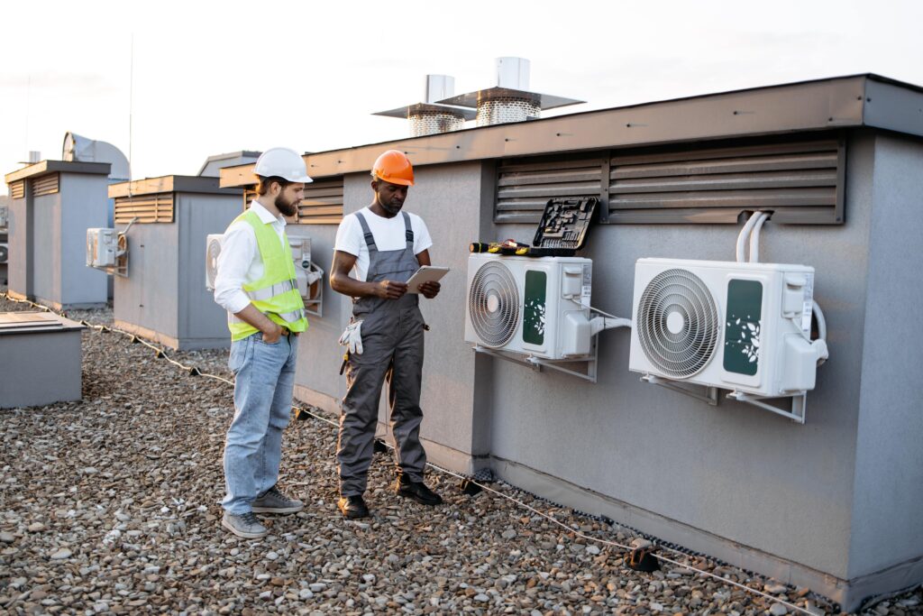 Diverse workers with tablet fixing air conditioner on plant